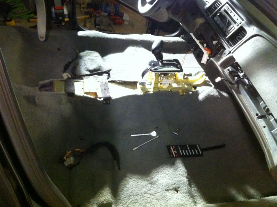 Interior of a car with the center console removed, showing the gear shifter and wiring