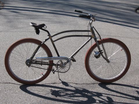 Old bicycle with brown tires and a bell on the front fork, parked on asphalt