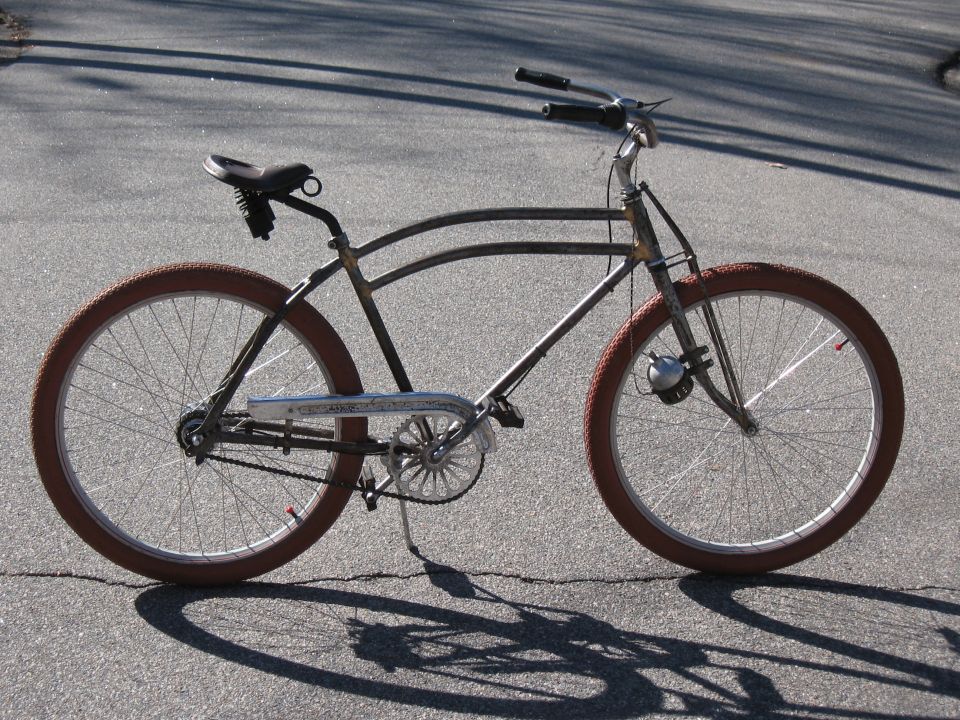 Old bicycle with brown tires and a bell on the front fork, parked on asphalt