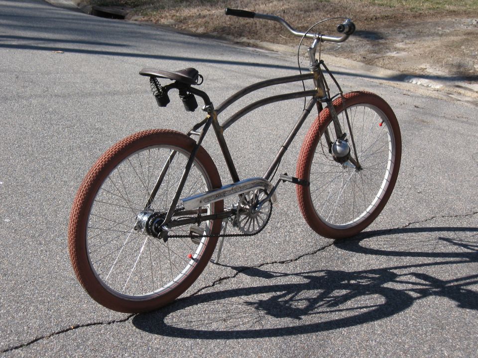 old bicycle with brown tires and a brown seat, parked on asphalt