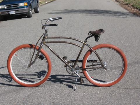 Rusty cruiser bike with orange tires parked on street, blue SUV in background