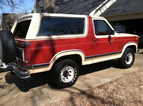 1986 Ford Bronco - This 1986 Ford Bronco features a classic two-tone red and cream paint scheme and a rear-mounted spare tire.