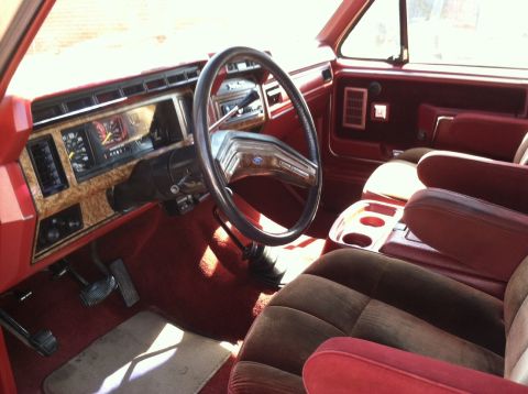 1986 Ford Bronco - The interior of the vehicle features a wood-grain dashboard, plush seating, and a center console with cup holders.