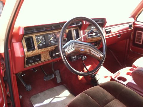 1986 Ford Bronco - The interior of a vintage Ford truck or SUV features a red dashboard and seats with wood grain accents.