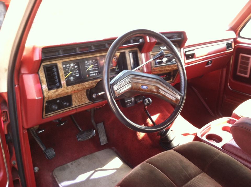 Red interior of a 1980s Ford truck or SUV, showing dashboard, steering wheel, and seats