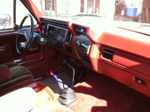 1986 Ford Bronco - The interior of a 1986 Ford Bronco features a red dashboard with wood trim accents and a prominent floor shifter.