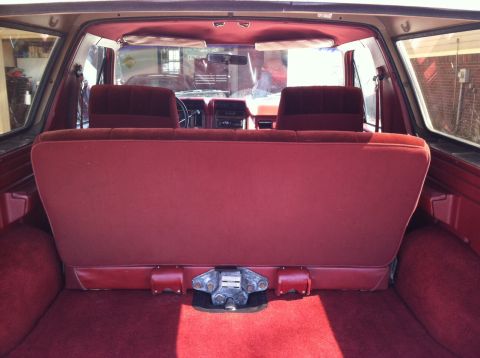 1986 Ford Bronco - The interior of a red SUV is shown from the back, a folded-down rear seat and a trailer hitch receiver.