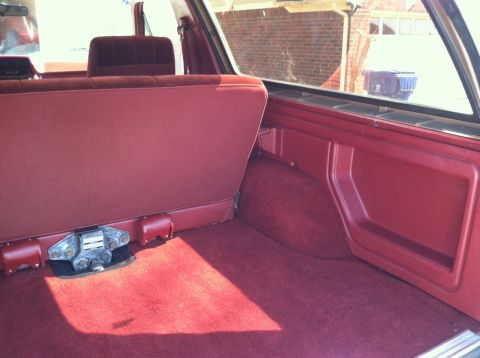 1986 Ford Bronco - The interior cargo area of a vehicle shows red carpeting and a folded rear seat.