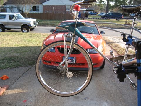 1994 Ford Bronco - A bicycle is positioned in front of an orange Ford Mustang, with a white Ford Bronco visible to the left.