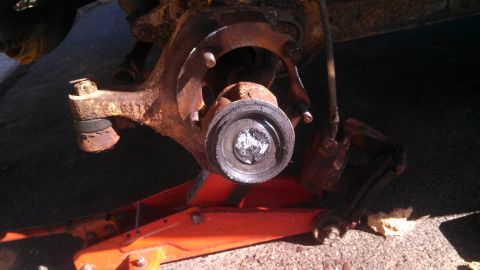 1979 Ford Bronco - Close-up of a heavily rusted vehicle suspension component being supported by an orange hydraulic jack.