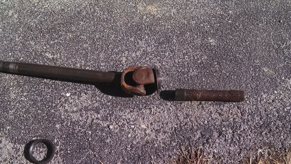 Driveshaft U-joint and a broken shaft piece on asphalt