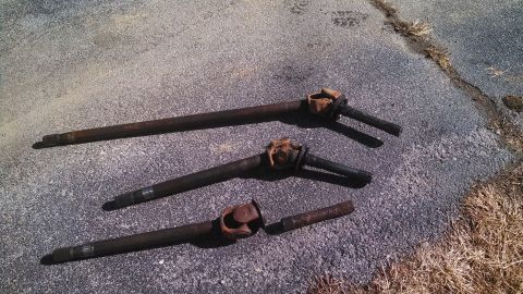 1979 Ford Bronco - Several driveshafts and a connecting piece lie on a paved surface, likely awaiting installation or repair.