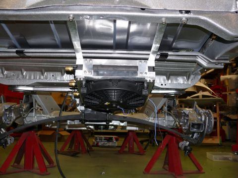 Undercarriage of a vehicle on jack stands, showing a cooling fan and leaf spring suspension