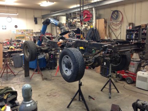 1993 Ford Bronco - The chassis of a vehicle is suspended on stands in a workshop, undergoing maintenance or repair.
