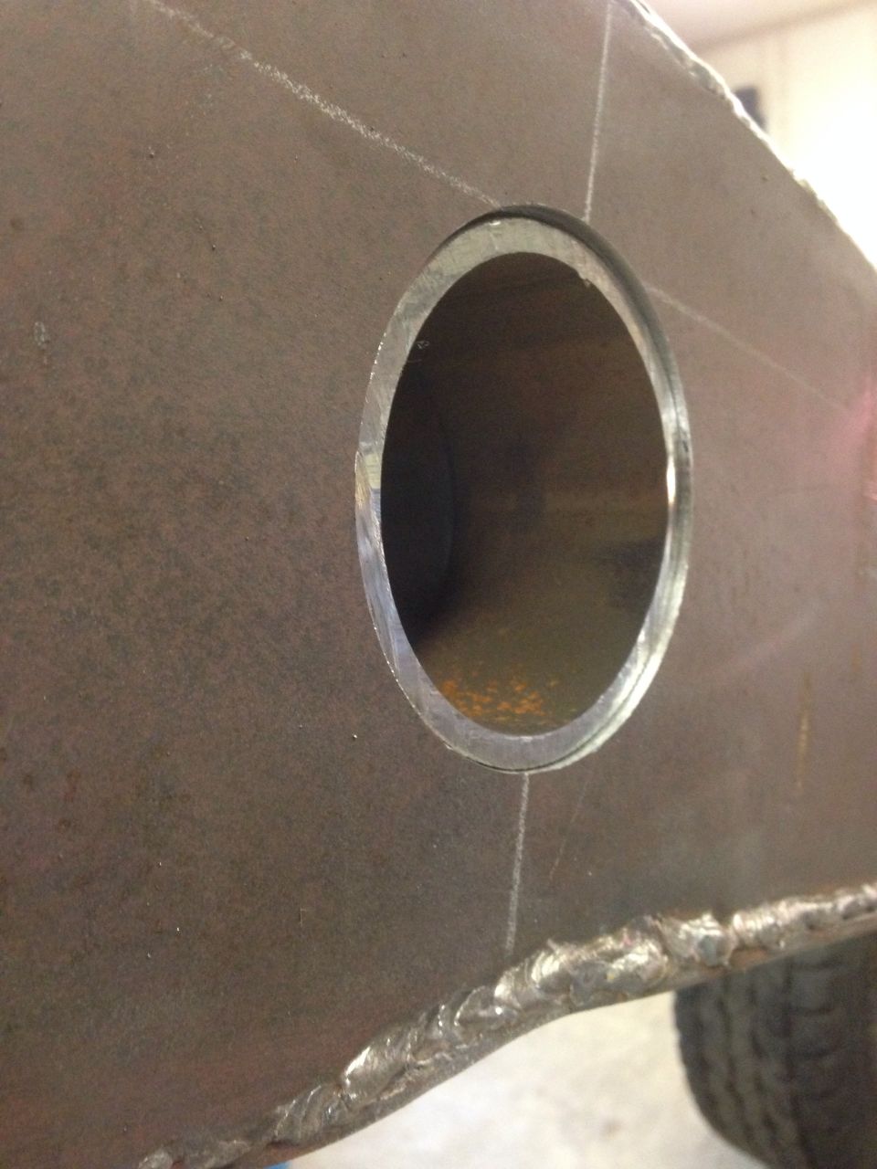 Close-up of a thick metal plate with a circular hole and visible weld seams