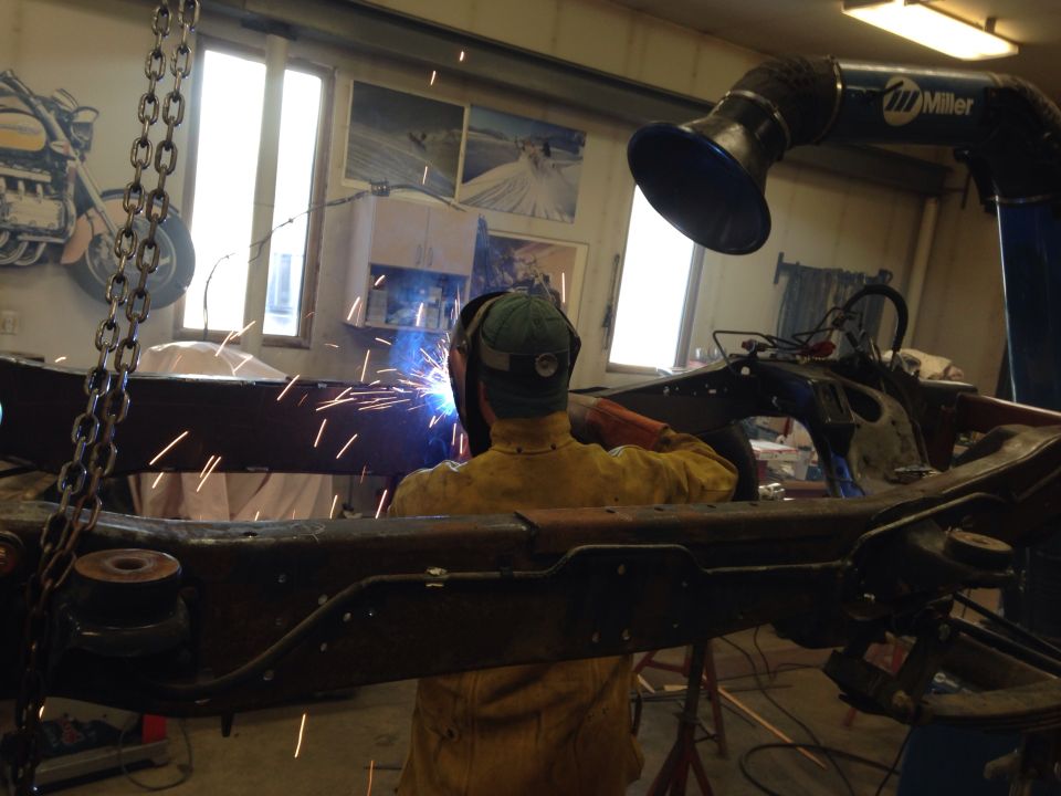Person welding a vehicle frame in a workshop. Miller exhaust hood overhead