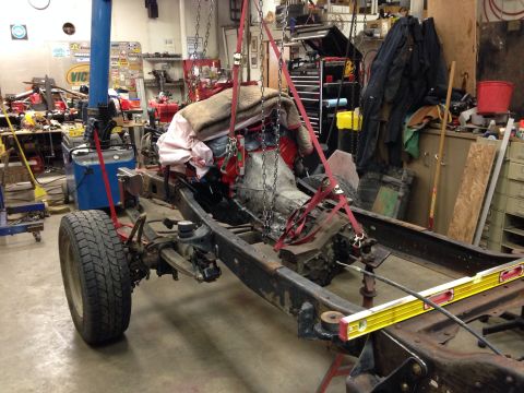 1993 Ford Bronco - A vehicle frame, engine, and transmission are being hoisted in a garage setting.
