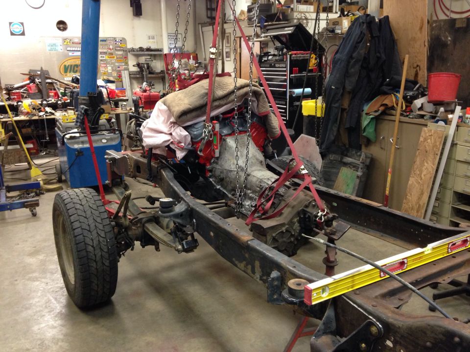 Vehicle frame with engine and transmission suspended by chains in a workshop