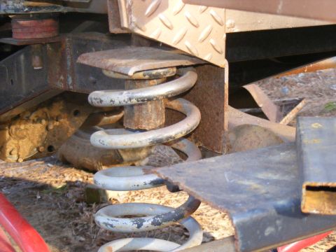 1978 Ford Bronco - Detail of a vehicle's suspension system, showing a coil spring and rusted metal parts.