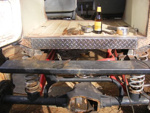 Rear axle and suspension of a vehicle being worked on, with tools and a beer on the bed