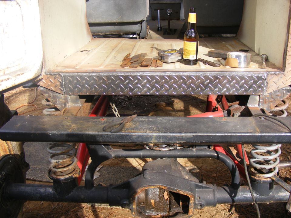 Rear axle and suspension of a vehicle being worked on, with tools and a beer on the bed