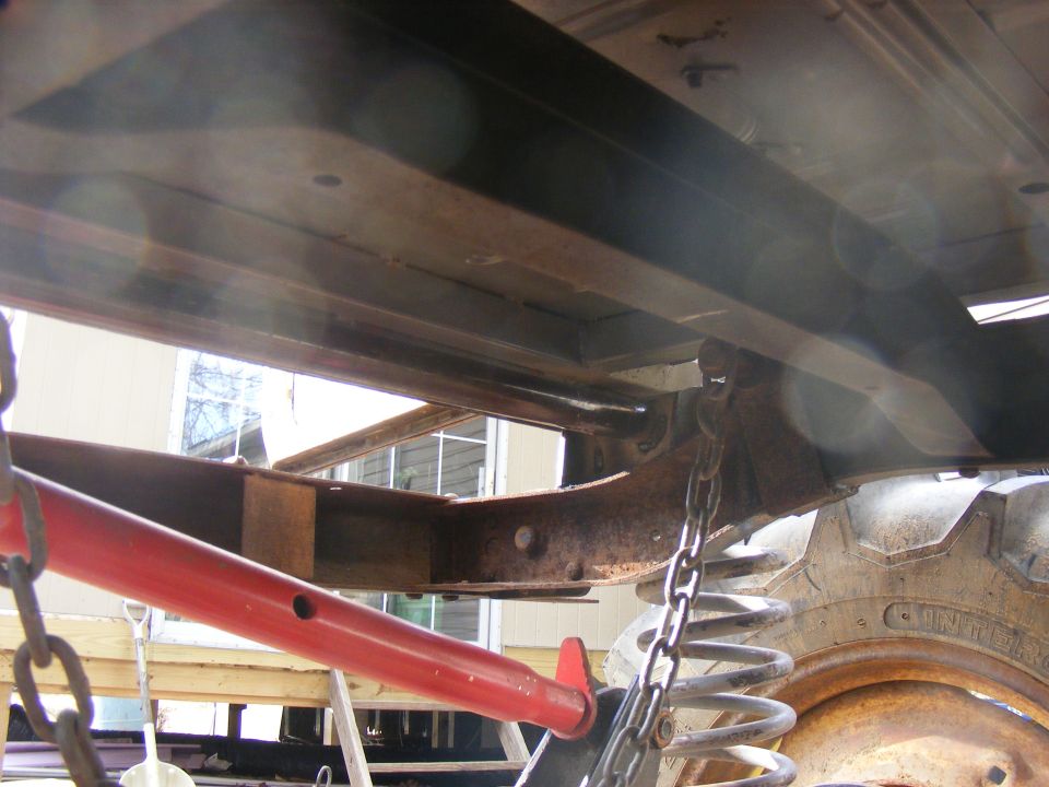 Close-up of vehicle undercarriage showing suspension components, a large tire, and red lifting equipment
