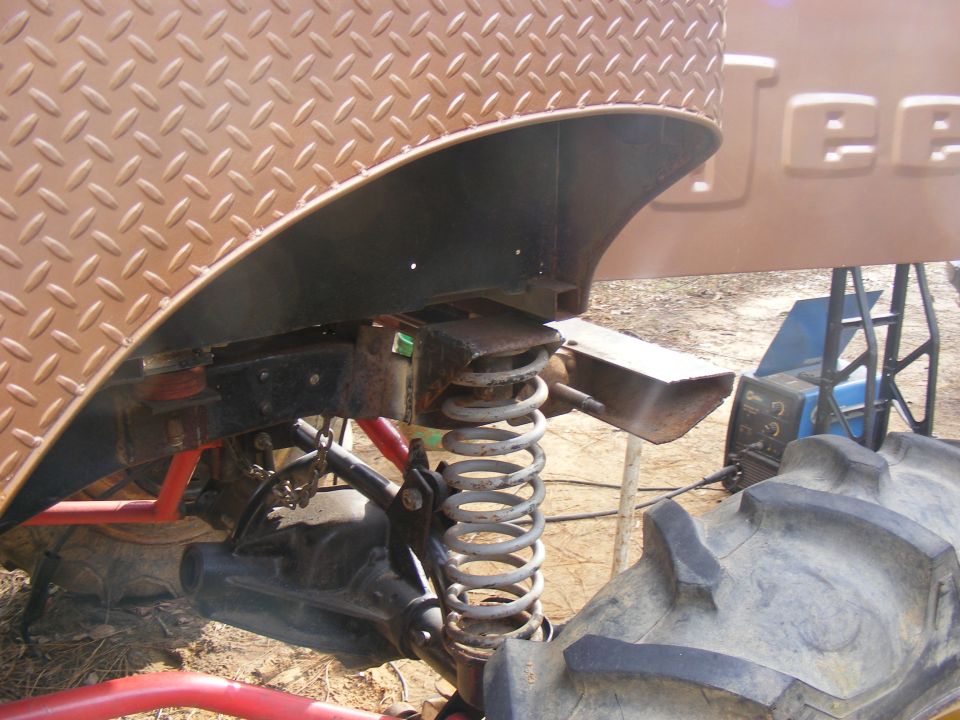 Brown diamond plate fender over a large coil spring and off-road tire