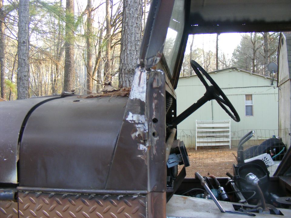 View of an old vehicle's interior showing the steering wheel, dashboard, and part of the hood. Diamond plate is visible on the lower body