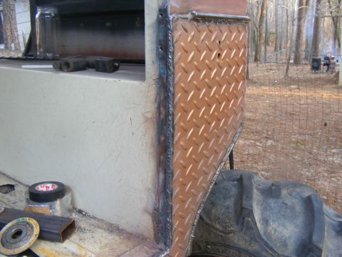Close-up of diamond plate and welded metal on a vehicle's exterior, with a large tire visible
