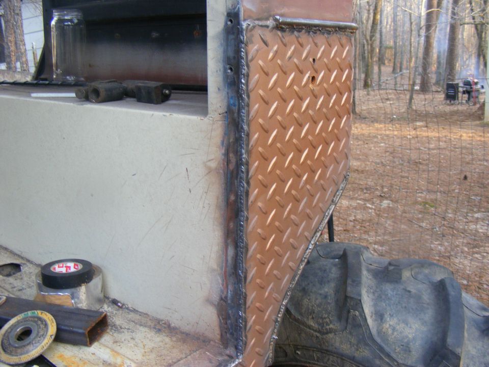 Close-up of diamond plate and welded metal on a vehicle's exterior, with a large tire visible