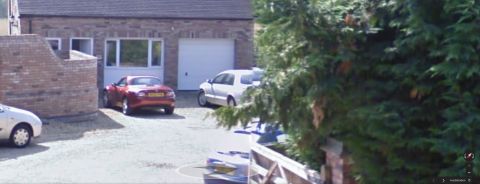 1999 Ford Fairlane - A red convertible and a white van are parked in front of a brick garage.