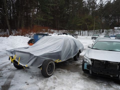2001 Ford Crown Victoria - A car is covered in plastic sheeting and parked in a snowy outdoor lot next to another vehicle.