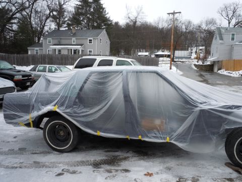 2001 Ford Crown Victoria - A car covered in plastic sheeting is parked on a snowy surface with other vehicles nearby.