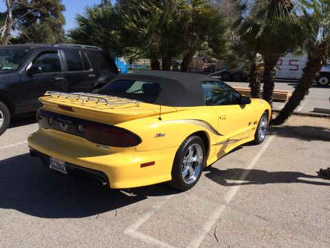 1968 Ford Mustang - A yellow convertible with a luggage rack on the trunk is parked next to a dark SUV.