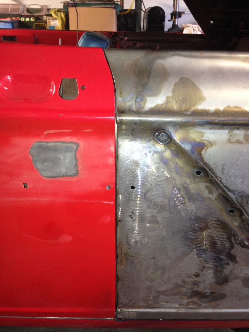 Red car door panel next to bare metal section with visible welds and bolt