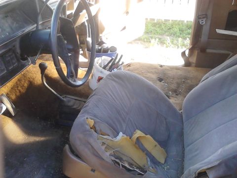 1990 Ford Bronco - The interior of an older vehicle shows a torn seat and a dashboard with a steering wheel and gear shifter.