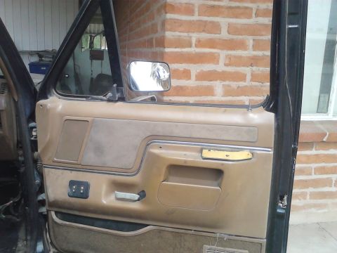 1990 Ford Bronco - Interior view of a vehicle's door panel, including the window crank and side mirror.