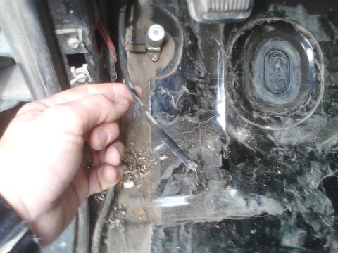 1990 Ford Bronco - Close-up of a hand manipulating wires inside a vehicle's footwell, with debris on the floor.