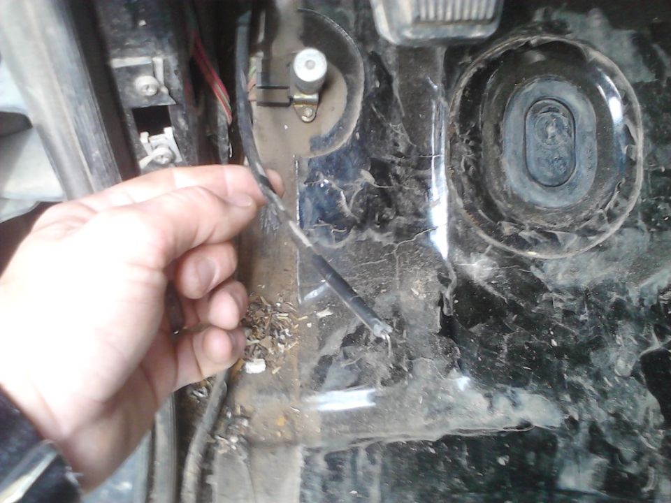 Hand holding frayed wire near vehicle pedals and floor mat debris