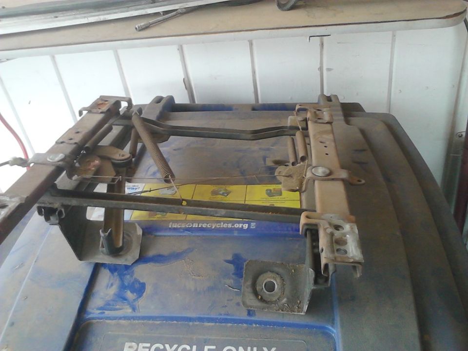 Rusty removed seat track and riser assembly with spring, sitting on a blue recycle bin lid