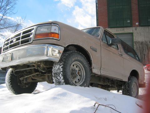 1996 Ford Bronco - A 1996 Ford Bronco sits partially buried in snow, with a brick building in the background.