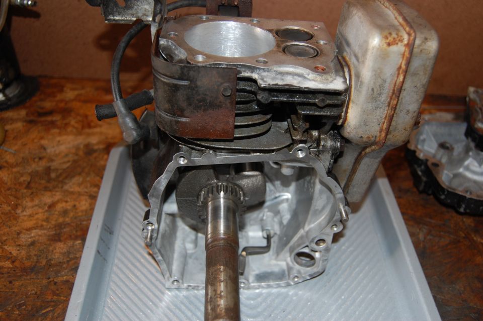 Engine block with crankshaft and muffler. The engine is disassembled and sits on a gray tray