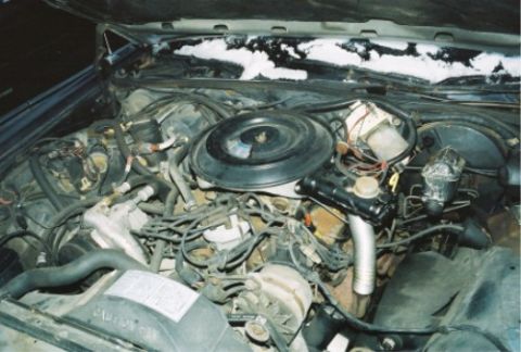 1984 Mercury Grand Marquis - The engine bay of a vehicle is shown with various components and wiring visible, with snow on the upper edge of the hood.