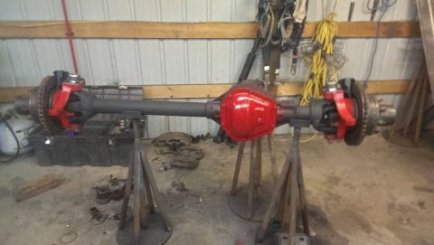 1995 Ford Bronco - A front axle assembly, likely for a truck or SUV, is displayed on stands with its differential housing painted red.