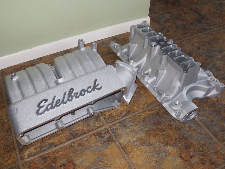 Two aluminum intake manifolds, one with 'Edelbrock' script, on a tiled floor