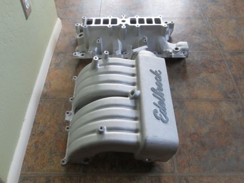 1996 Ford Bronco - Two aluminum intake manifolds are shown on a tiled floor. One has the Edelbrock brand name visible.