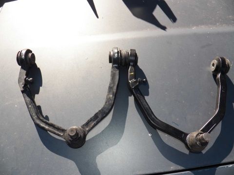 1998 Lincoln Mark VIII - Two black front suspension control arms are shown laid out on a gray surface.