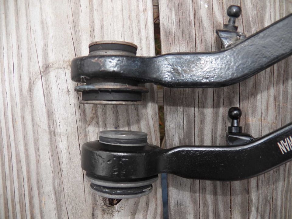 Two black metal front suspension control arms with rubber bushings and ball joints, one above the other