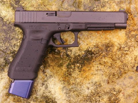 1996 Ford Bronco - A black Glock pistol with an extended blue magazine base plate rests on a textured surface.
