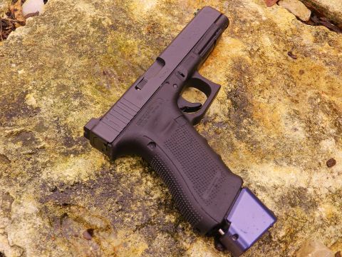 1996 Ford Bronco - A black Glock pistol with an extended purple magazine rests on a textured rock surface.